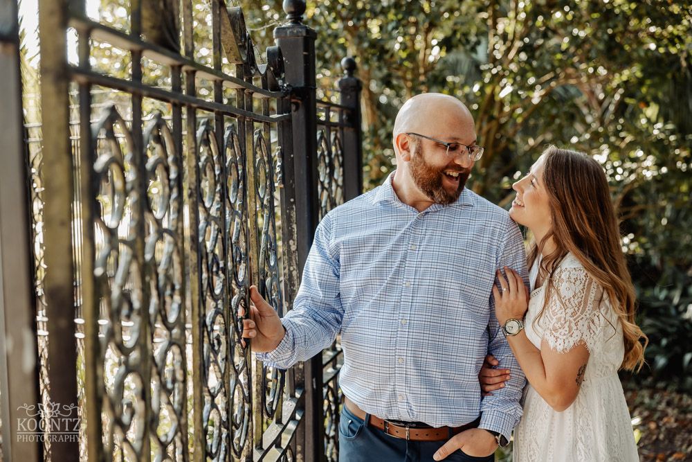 A playful engagement photo of a couple posing by an ornate iron fence.
