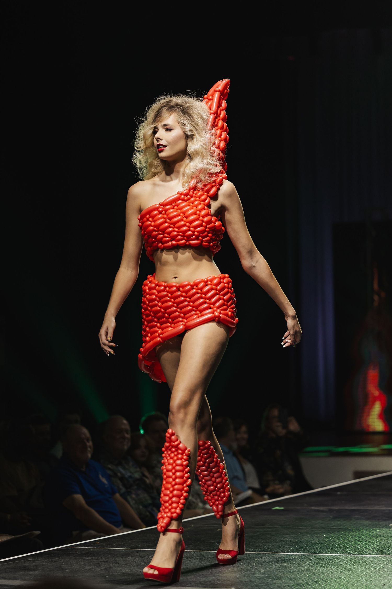 Model walks runway in striking red balloon-sculpted crop top, mini skirt, and hat ensemble.