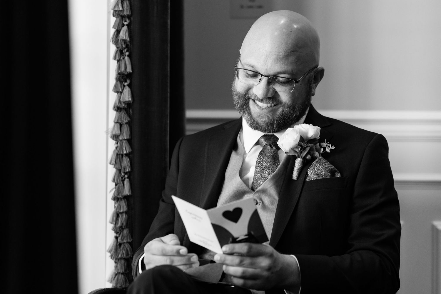 Black and white photo of smiling bald groom reading a heartfelt wedding card.