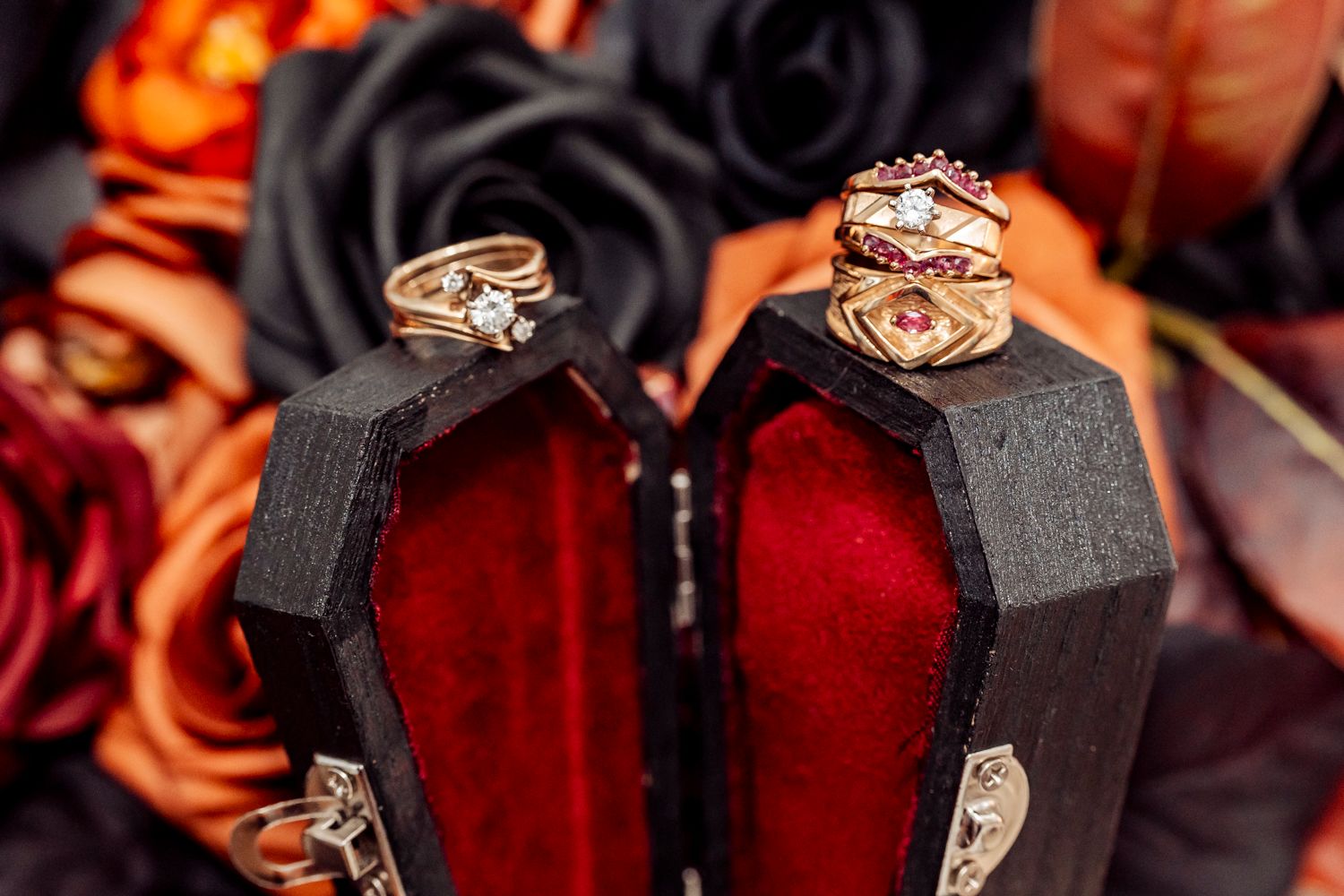 Gothic coffin ring boxes displaying elegant gold engagement and wedding rings with dark floral backdrop.