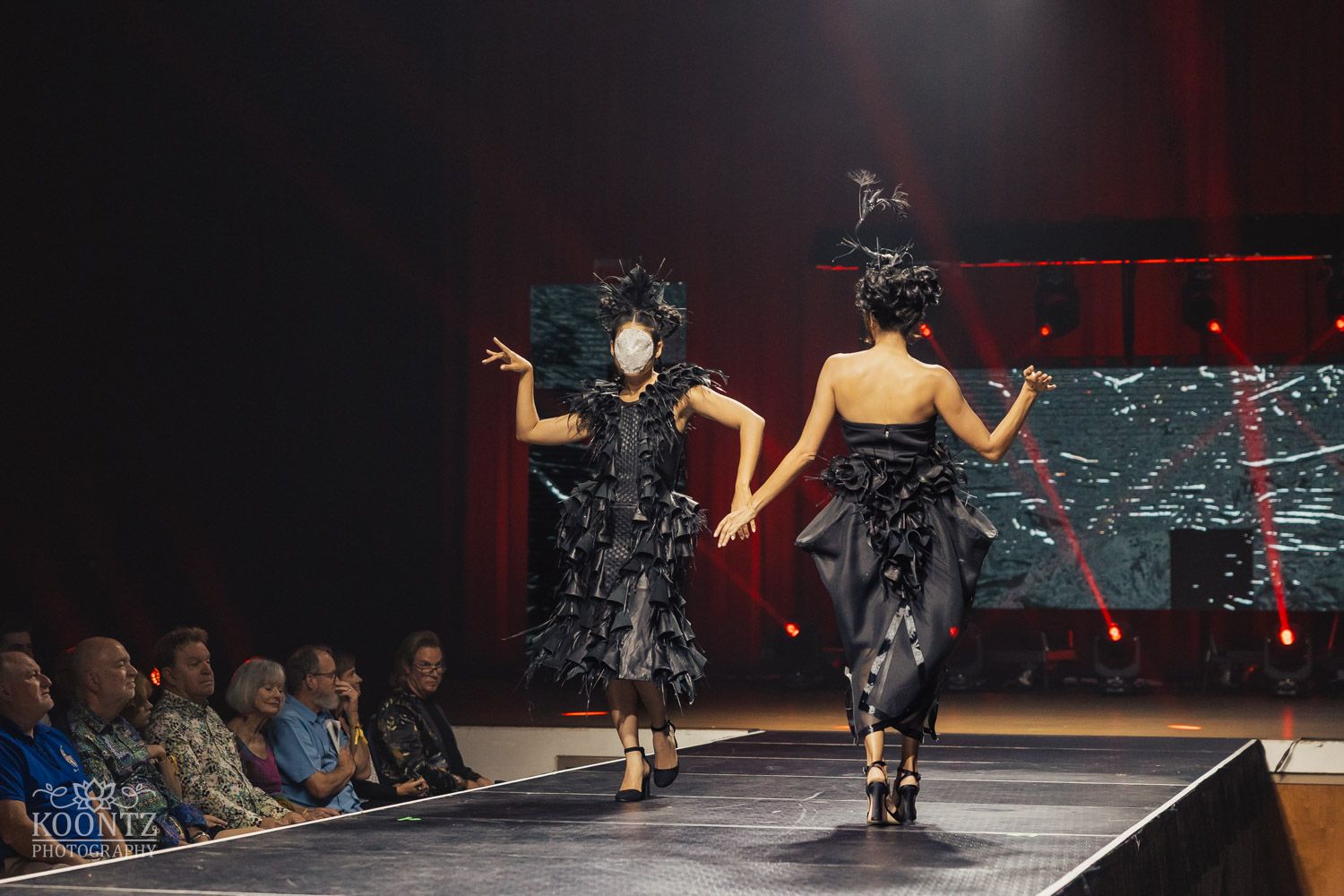 Modern dance performance on stage with dramatic lighting and audience silhouettes.