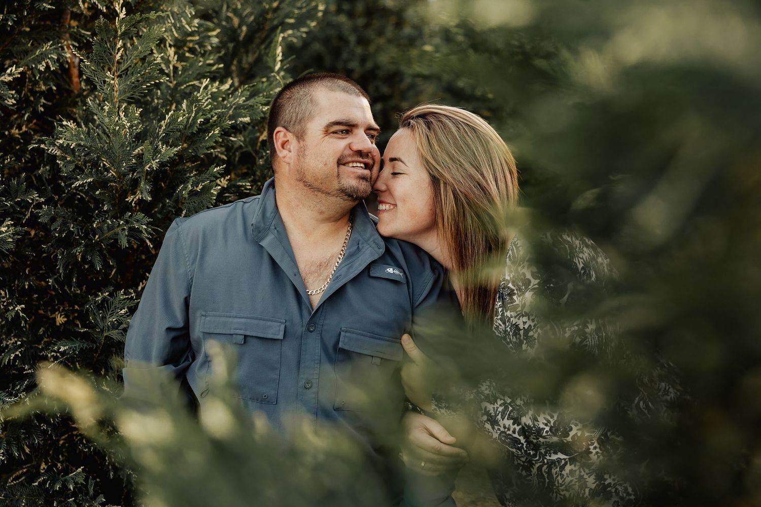 Romantic couple sharing a tender moment surrounded by dense green foliage, man smiling warmly.