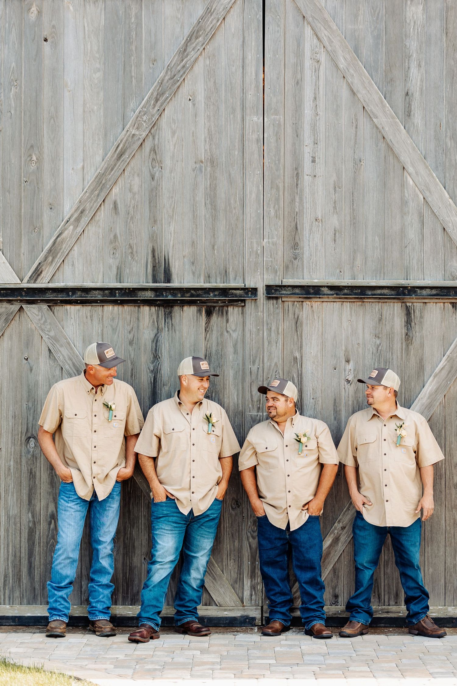 Four people in matching outfits lean casually against a rustic barn door.