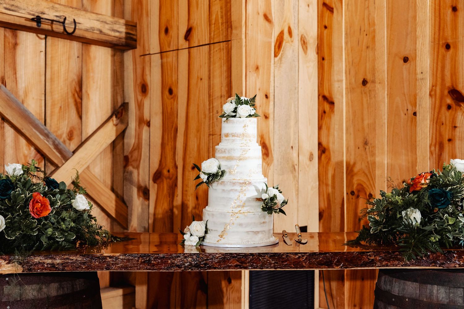 Simple elegant white wedding cake displayed on rustic wooden table with floral decorations.