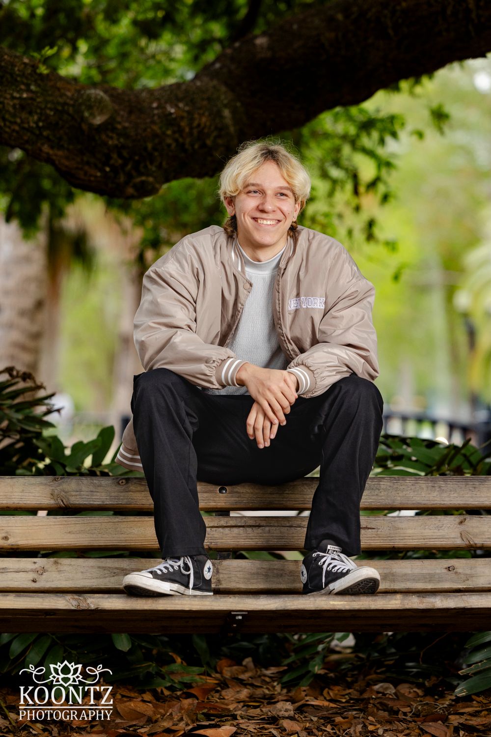 Casual outdoor portrait session on a wooden bench with lush greenery backdrop.