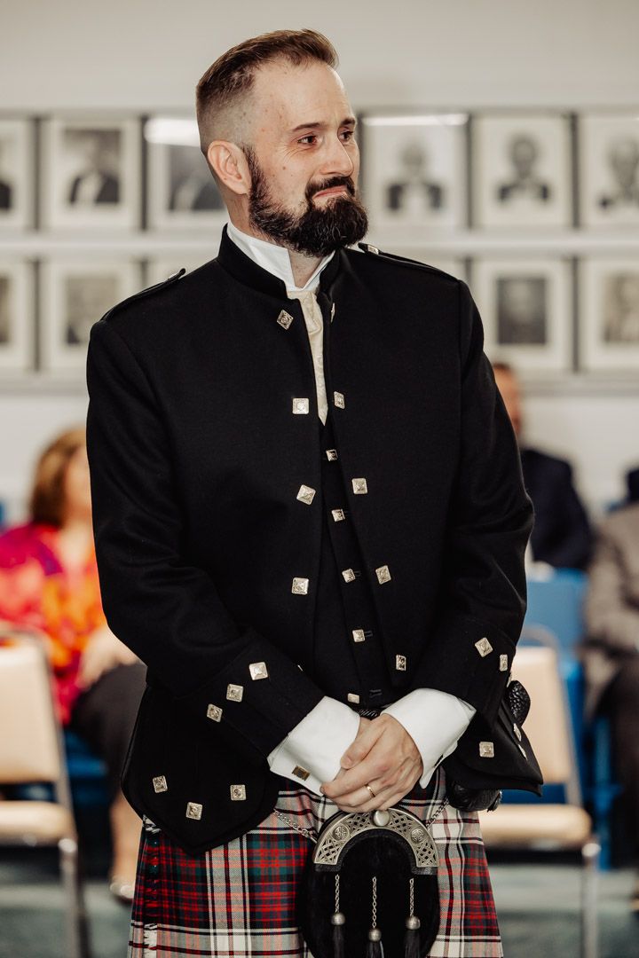 A person wearing traditional Scottish formal attire with detailed silver buttons and kilt.