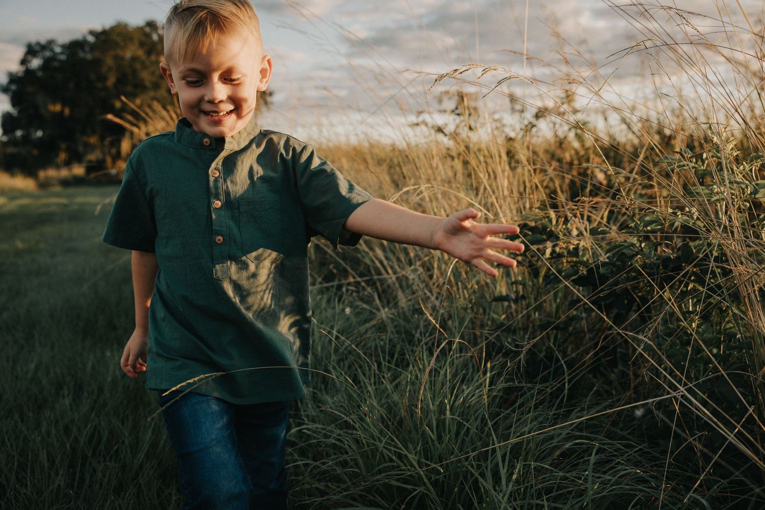 A child in green shirt and jeans plays outdoors in golden evening light.