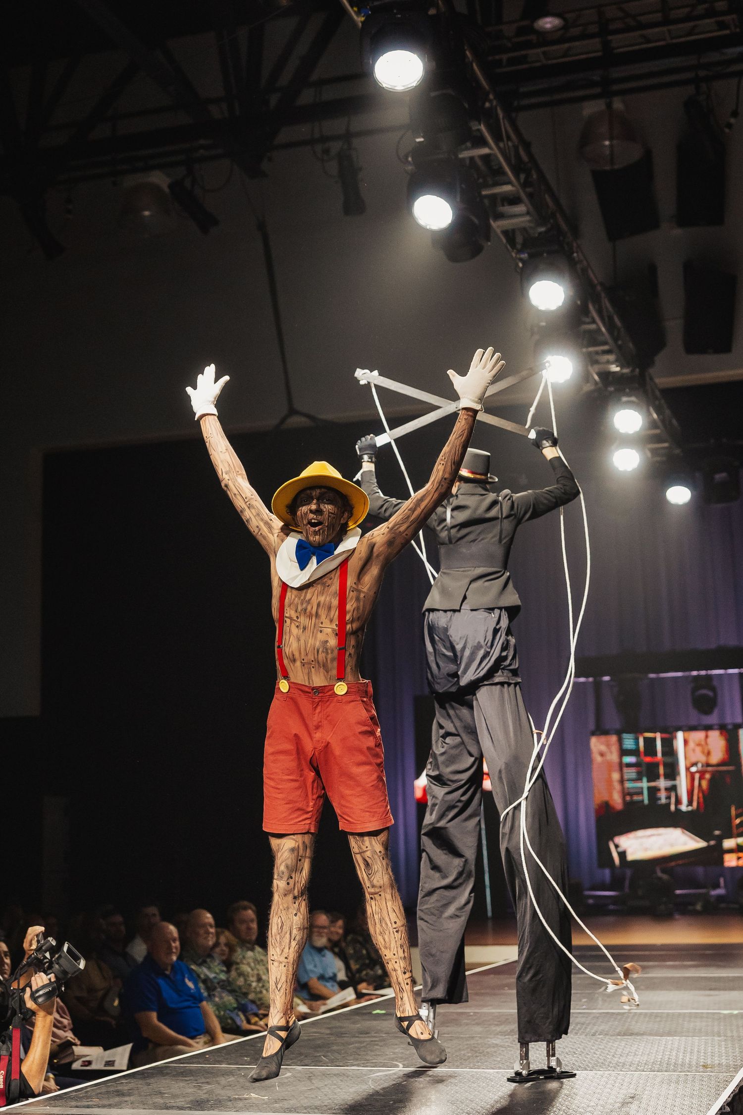 Performer dressed as Pinocchio with puppet strings on stage at a fashion show.