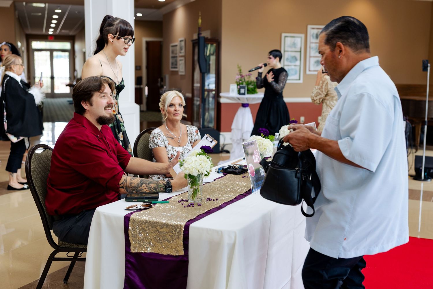 Guests and staff interact at a registration table during a formal event with elegant table settings.
