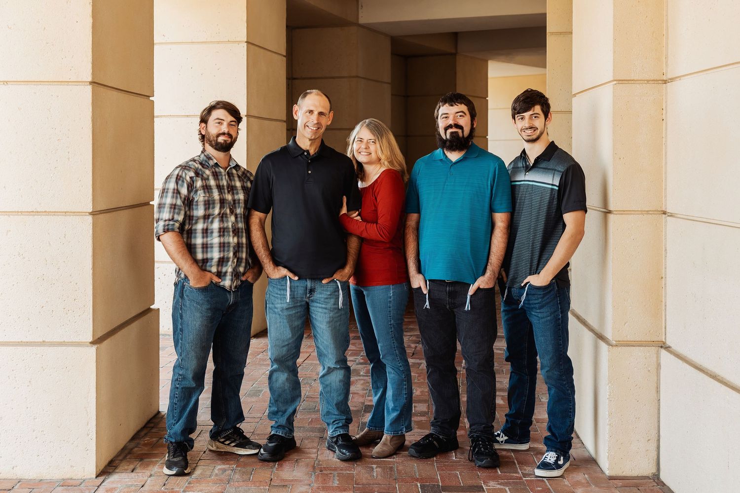 Family of five adults posing together in an outdoor architectural corridor setting.