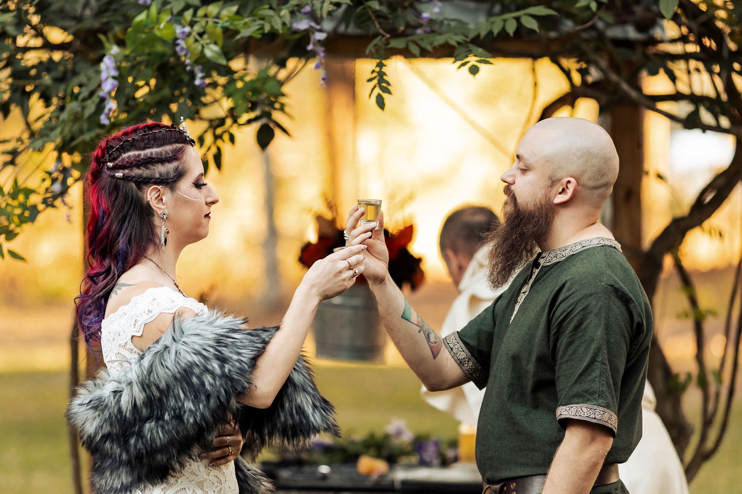 Bride and groom in Viking attire share ceremonial drink toast under floral arch at wedding.