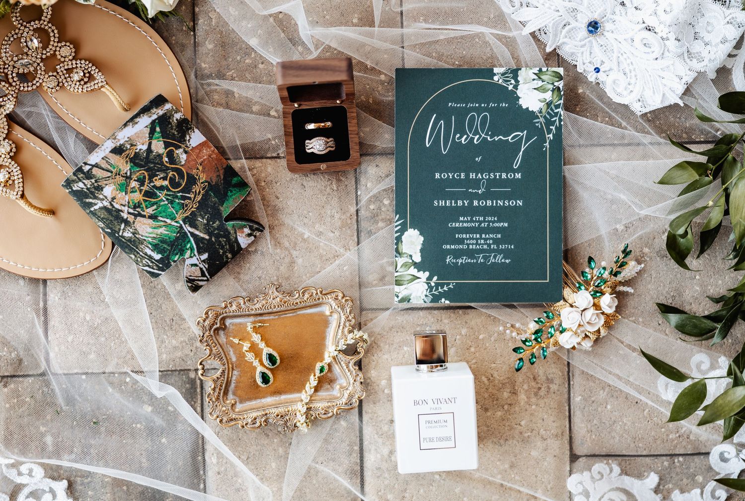 Wedding details flatlay with teal invitation, perfume, jewelry and floral elements.