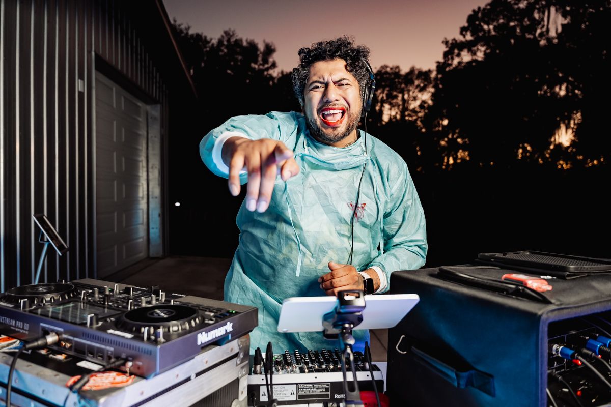 Energetic DJ in scrubs costume performing at an outdoor Halloween wedding reception at dusk.