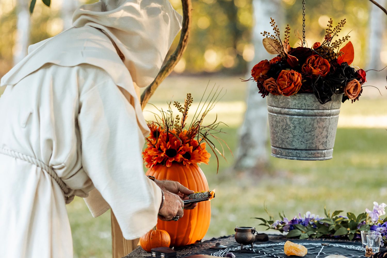 Person in white robe arranging autumn floral decorations outdoors.