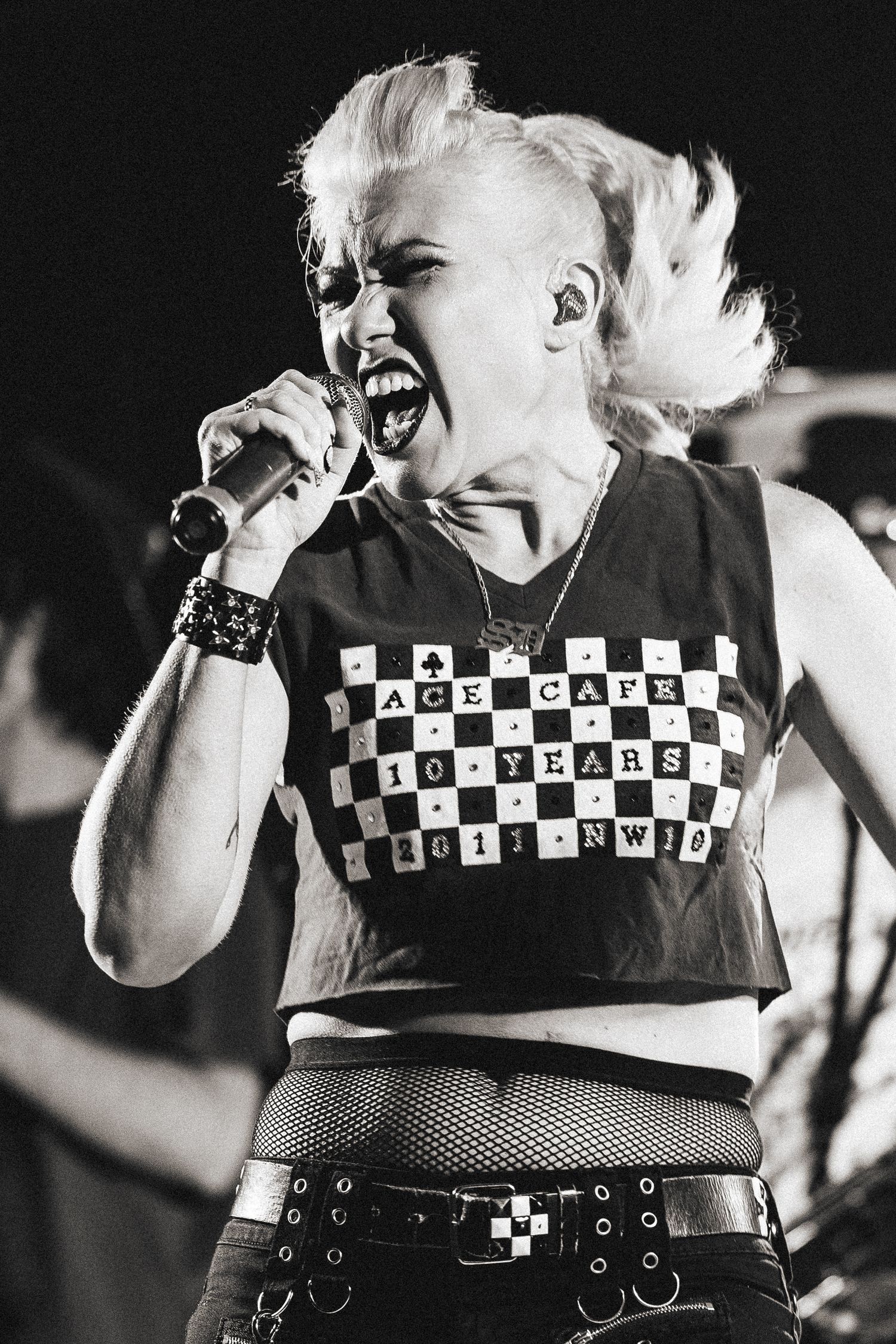Blonde female punk singer screams into microphone wearing Ace Cafe 10 Years shirt.