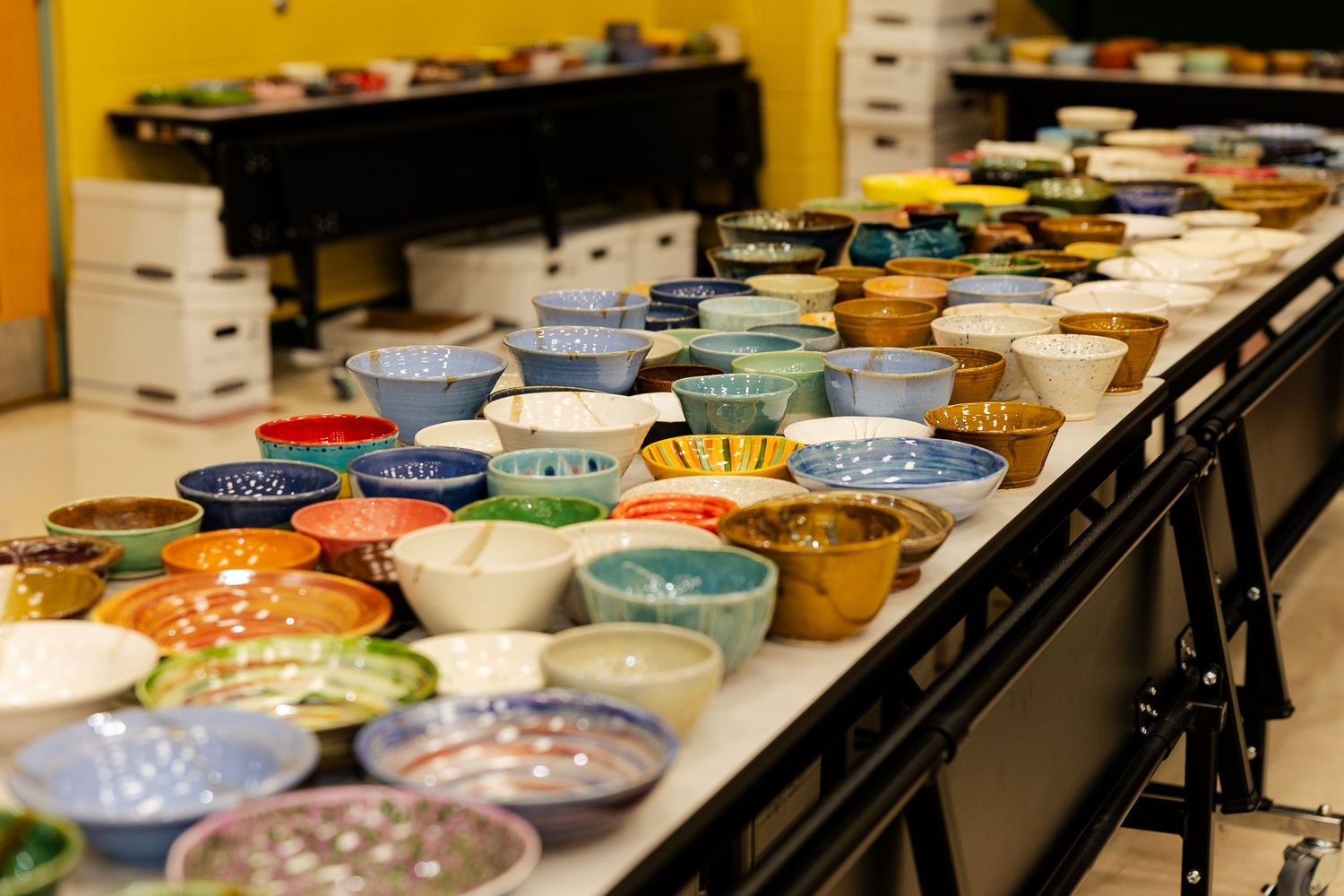 Long table filled with rows of colorful handcrafted ceramic bowls at a fundraising event.