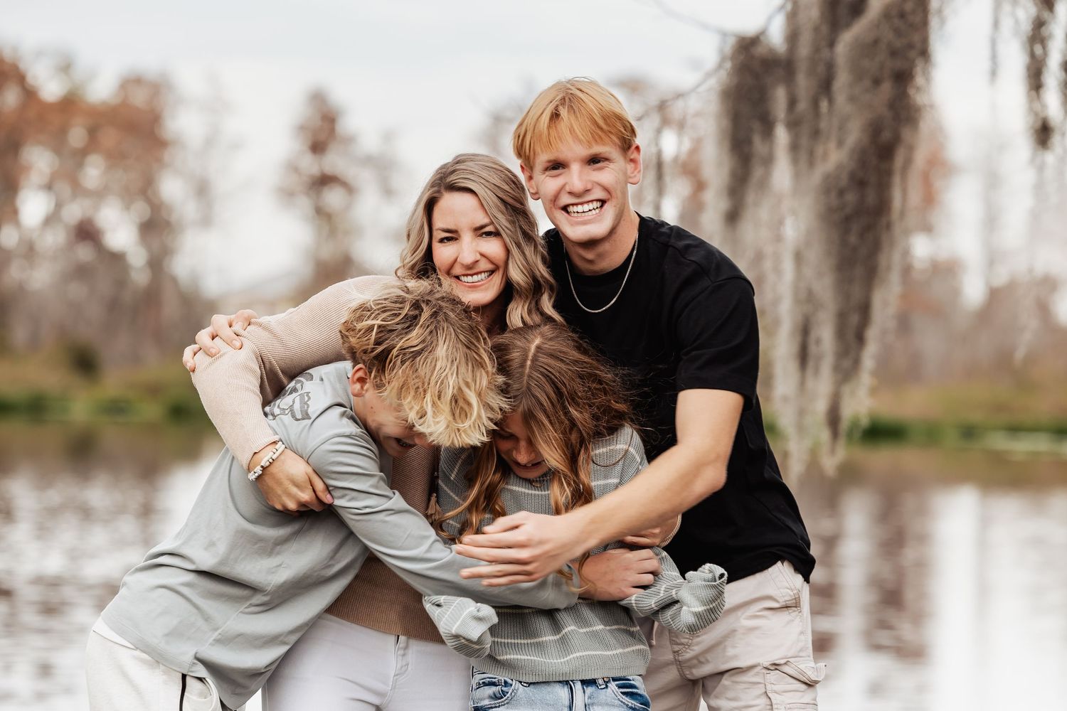 Joyful family group hug and laughing together outdoors near a scenic lake.