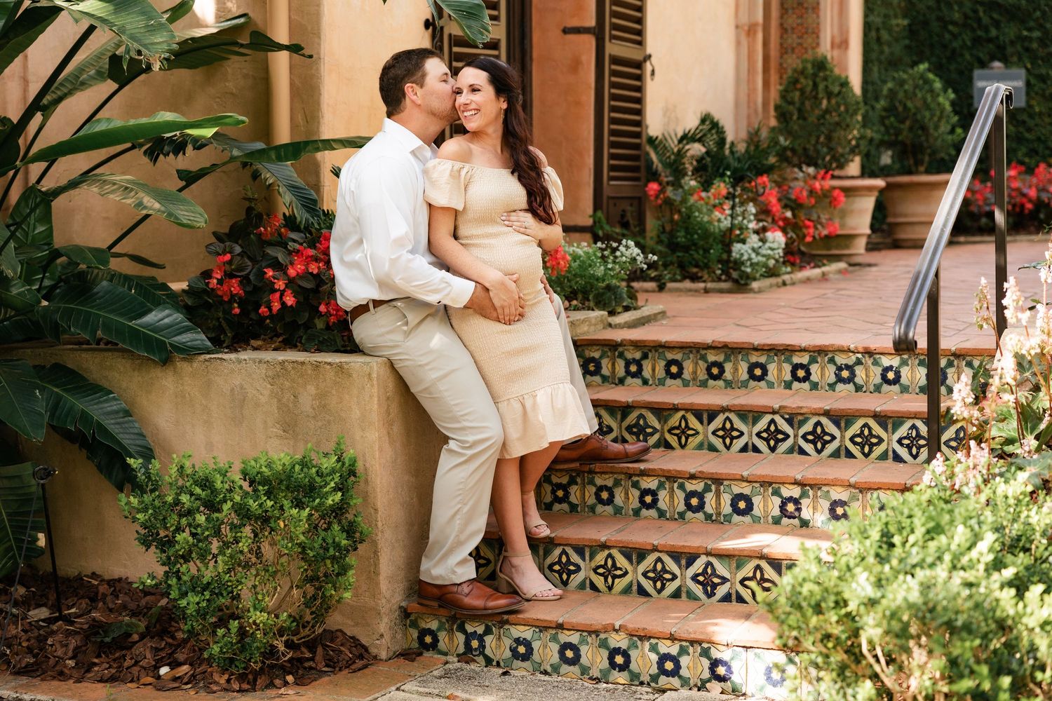 Couple sitting on decorative tiled steps, pregnant woman in elegant beige dress.