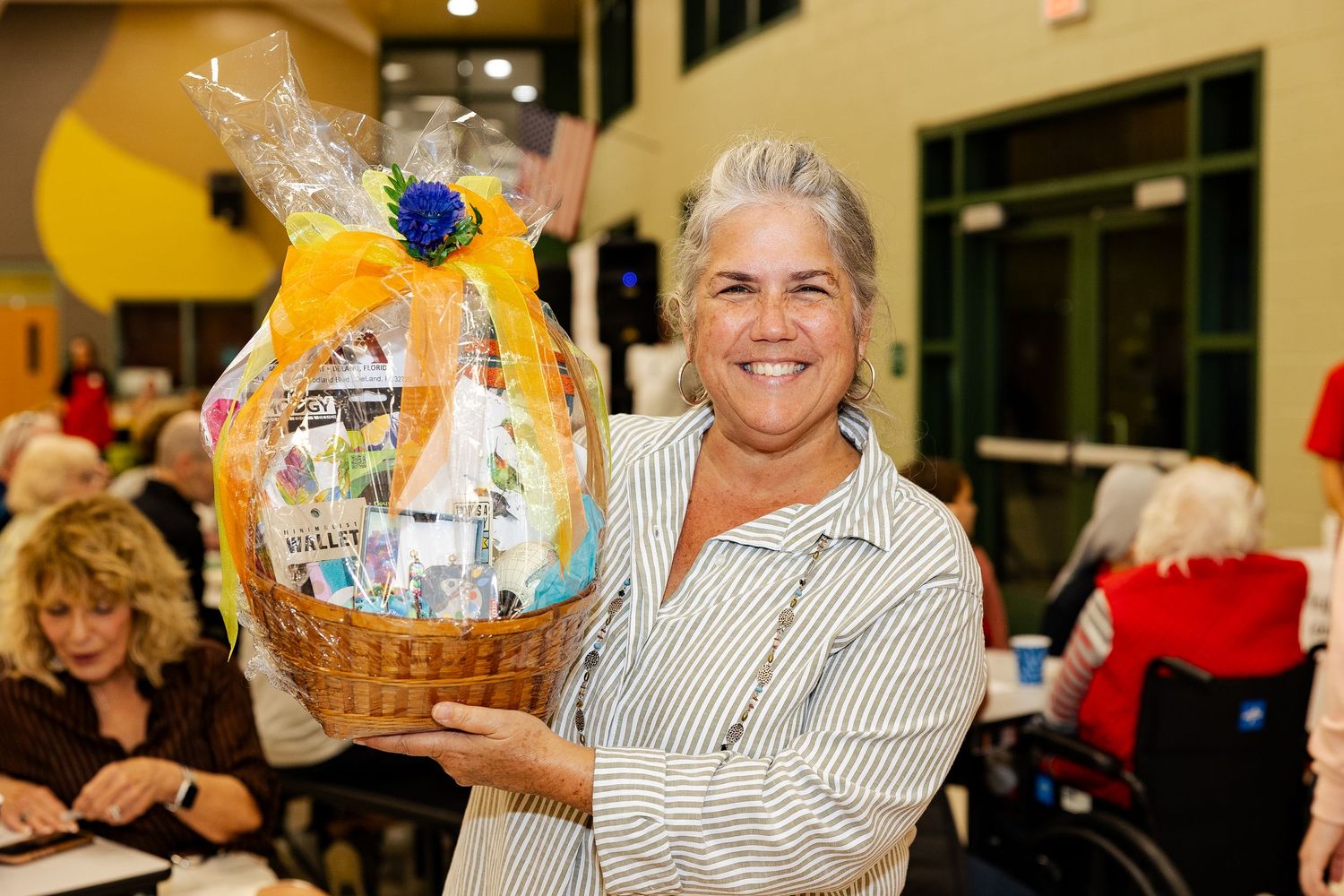 Smiling woman proudly holding a large gift basket filled with products at a charity event.