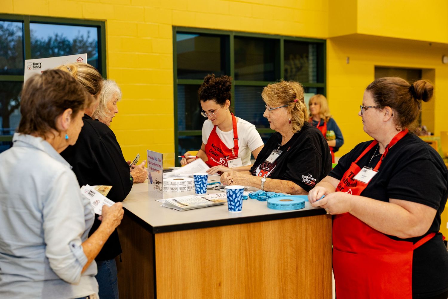Volunteers in red aprons assist guests at a registration table during a community fundraising event.