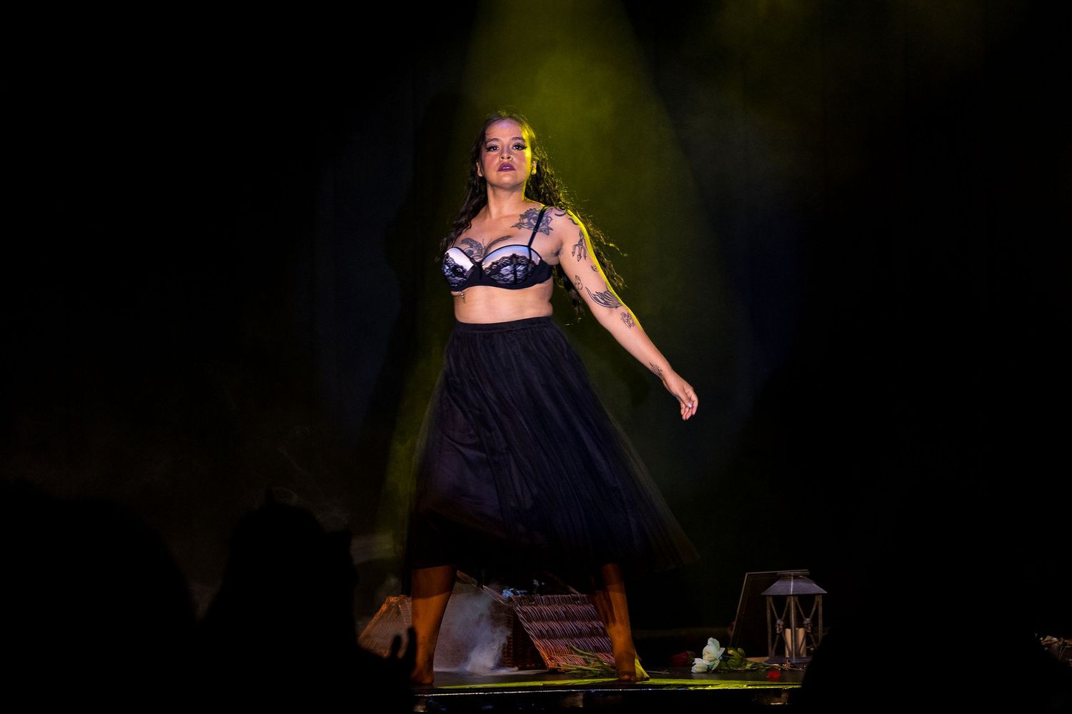 Tattooed burlesque performer in navy bra and black tulle skirt standing on stage table.