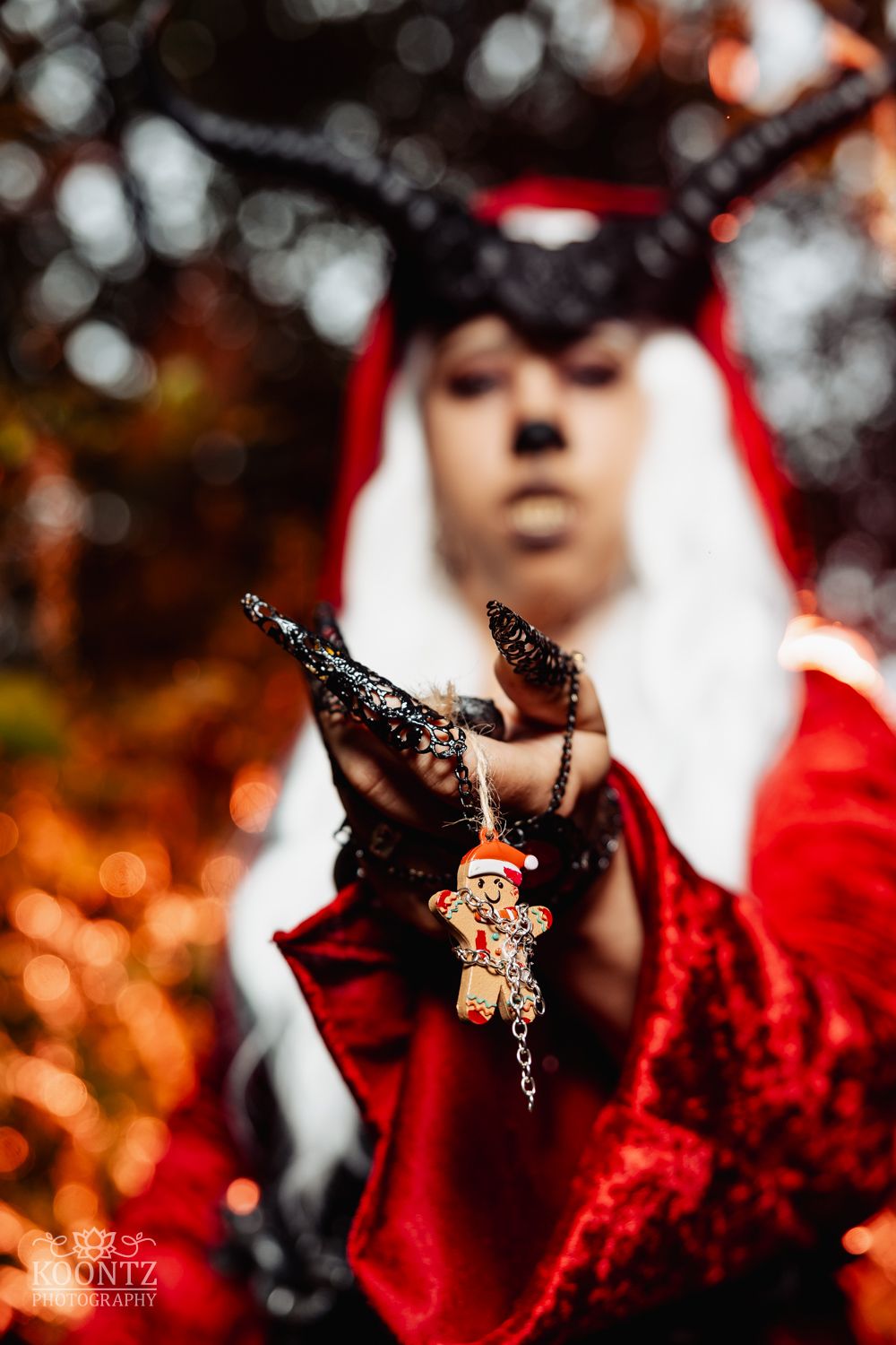 A close-up of a cosplayer with black horns holding a gingerbread man ornament with long black glittery nails.
