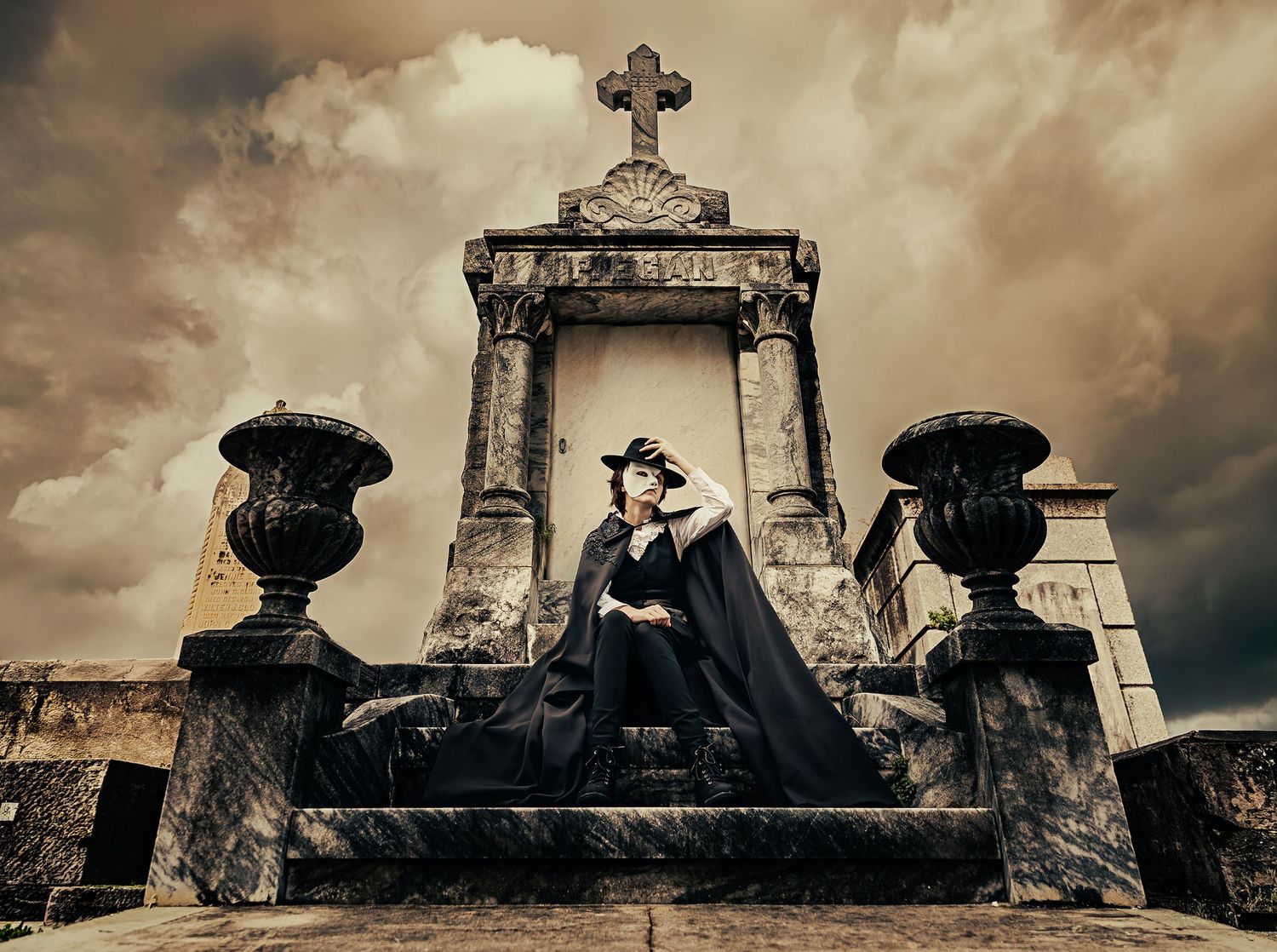 Gothic woman in black dress and hat sits on ornate stone tomb in dramatic cemetery under stormy sky.