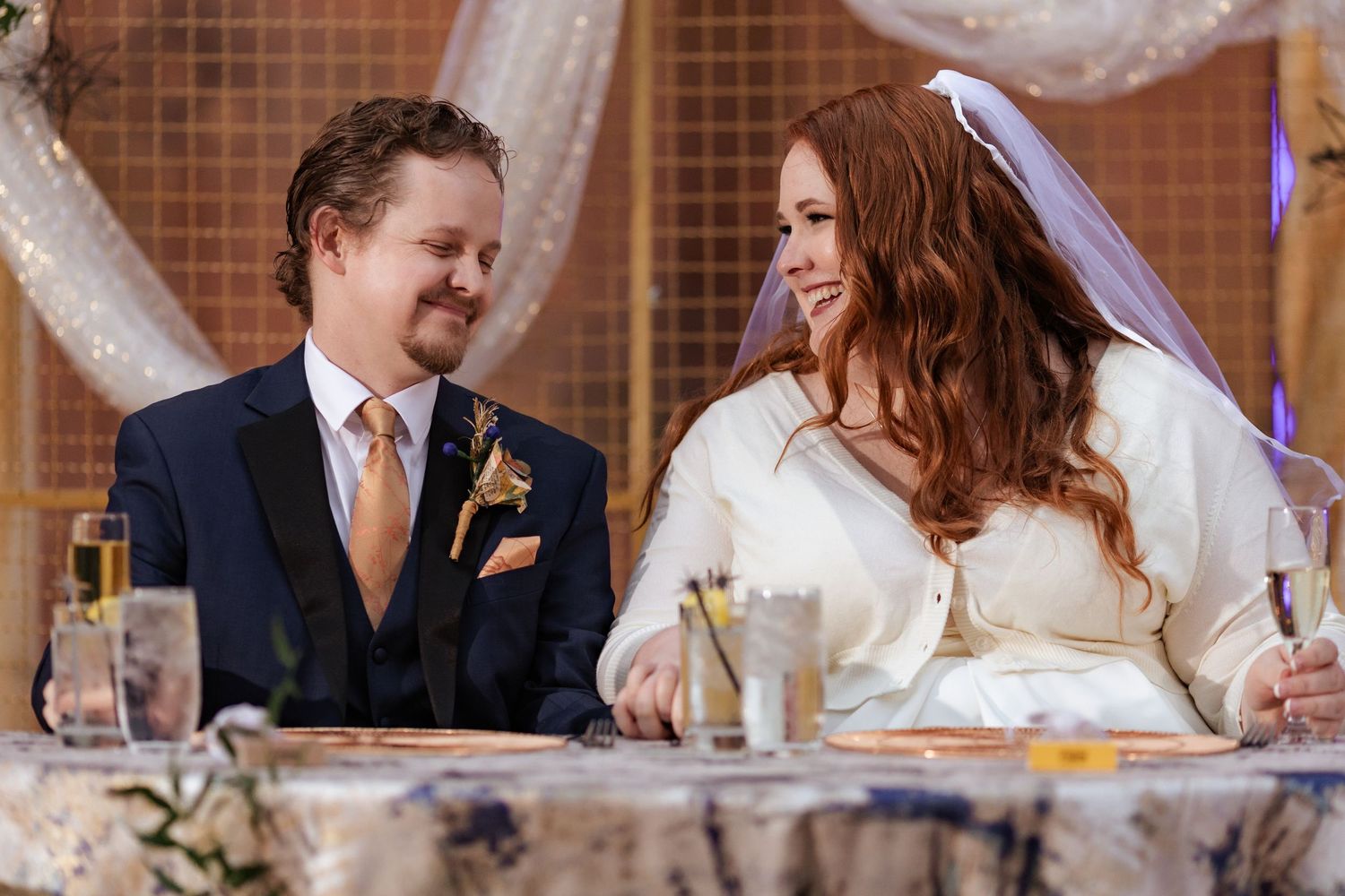 Bride and groom laughing together at sweetheart table during wedding reception.