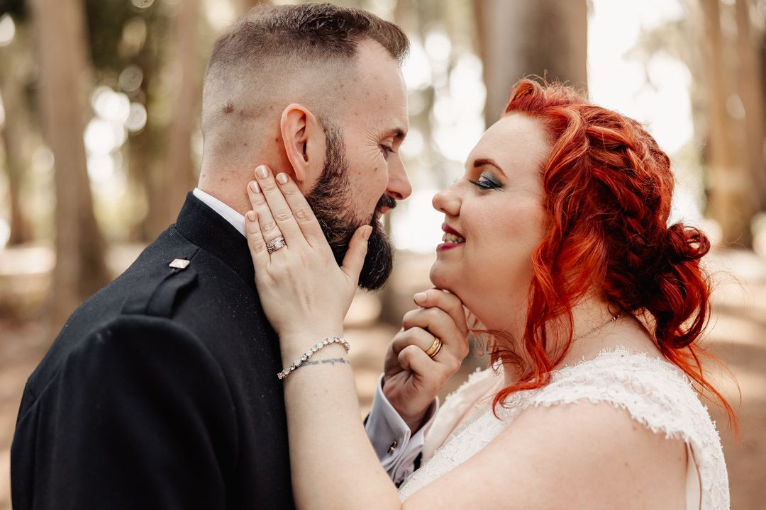 Bride with red hair and groom sharing romantic moment outdoors at wedding.