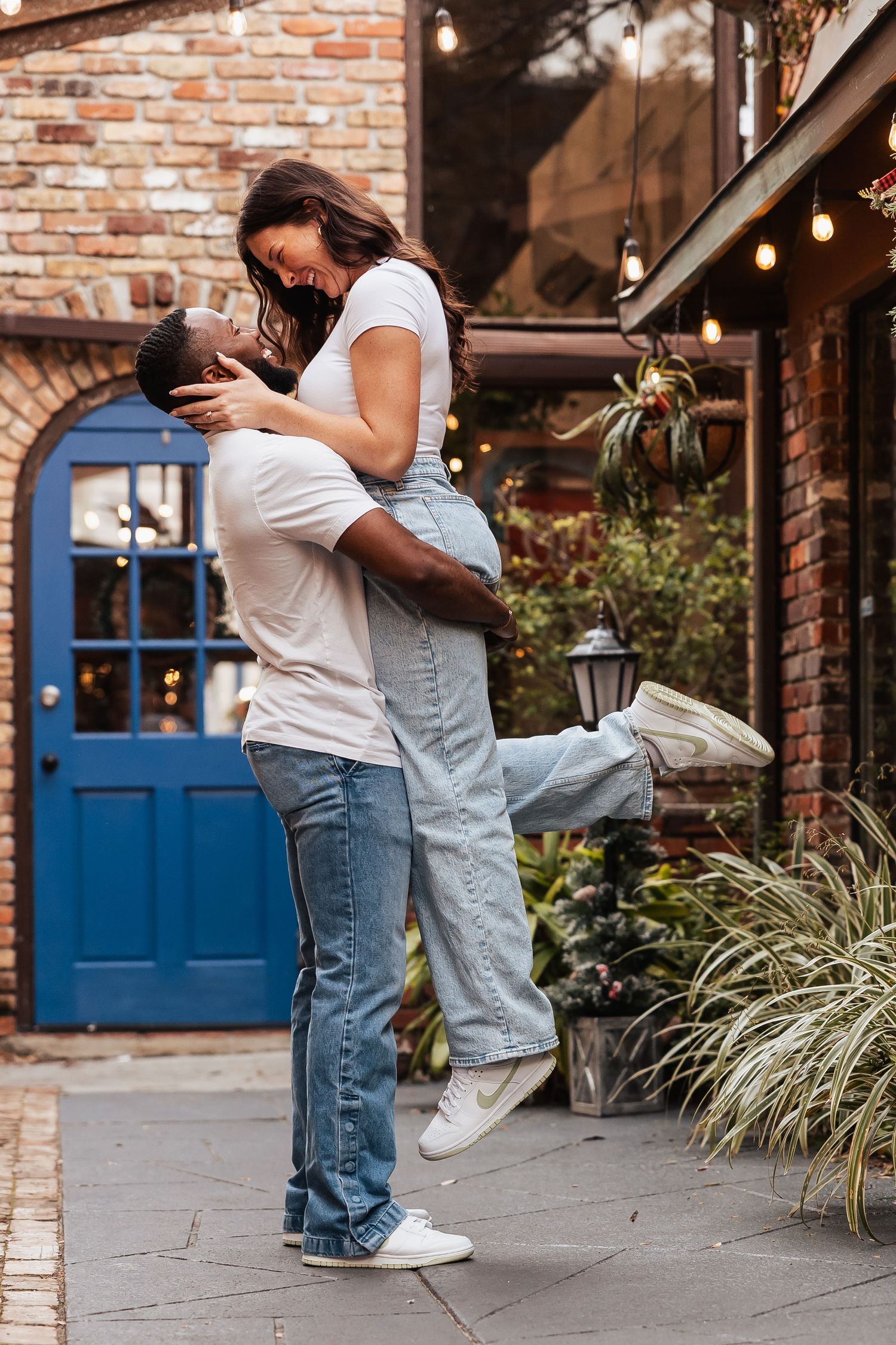 Romantic couple embracing while one is lifted up in front of rustic brick courtyard.