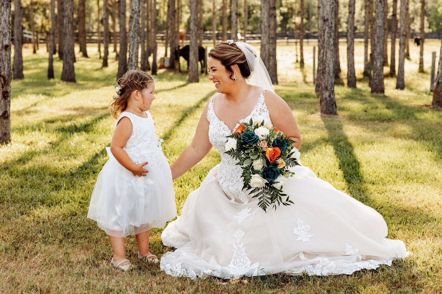 Sweet moment between bride and flower girl in matching white dresses outdoors.