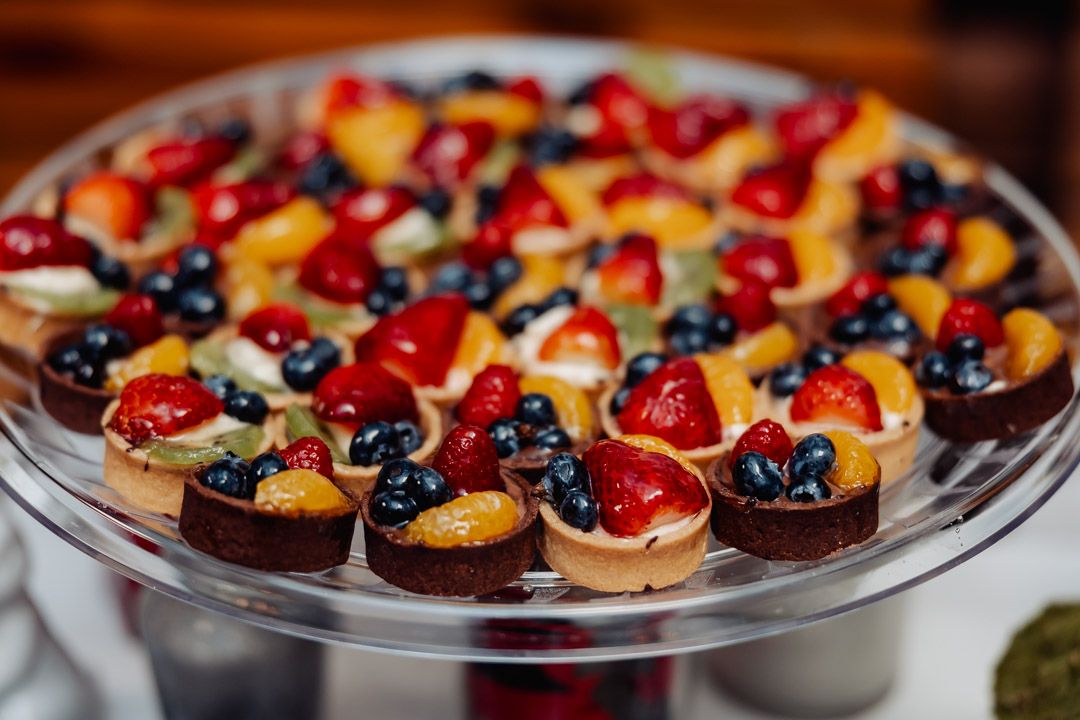 Colorful fruit tarts beautifully arranged on a clear glass serving platter.