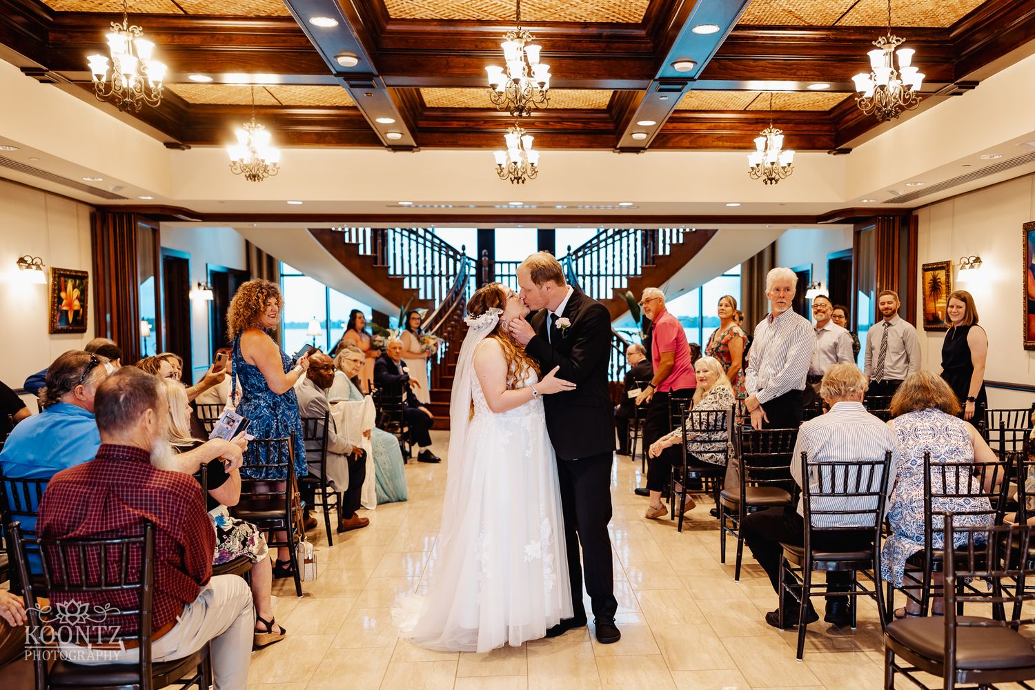 Wedding reception in an elegant ballroom with chandeliers and dark wooden details.