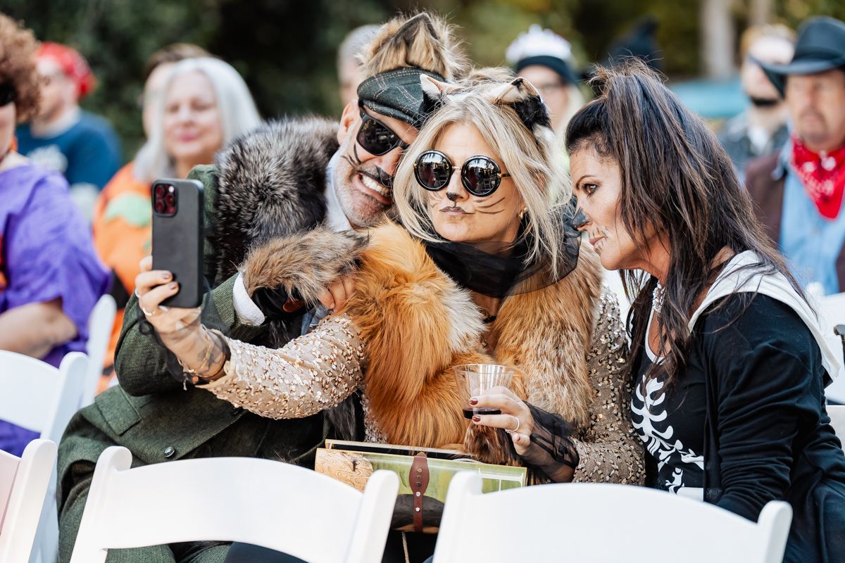 A crowd of people wearing sunglasses and costumes gather outdoors at a festival or event.