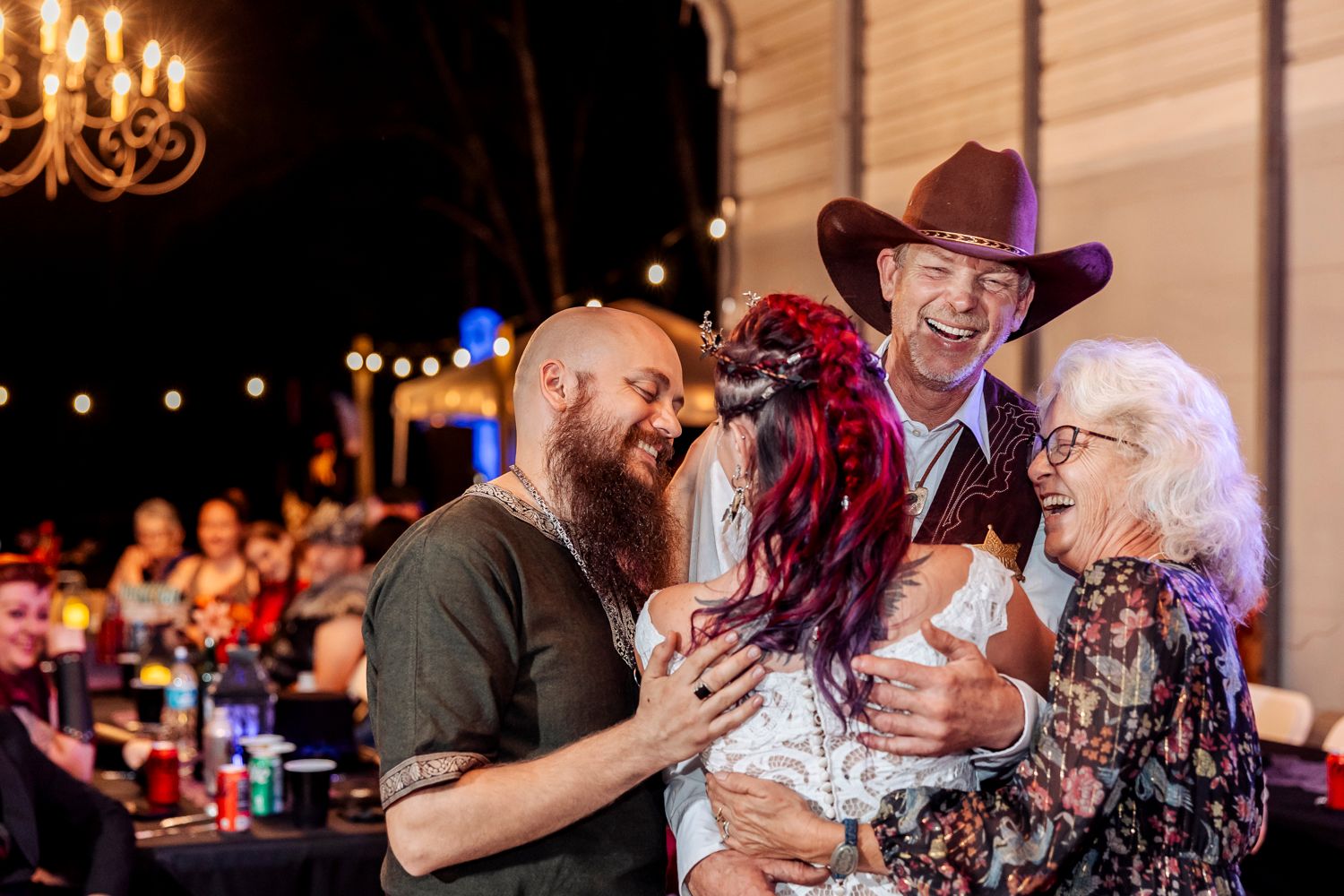 Wedding celebration featuring three generations sharing drinks and laughter under warm chandelier lighting.