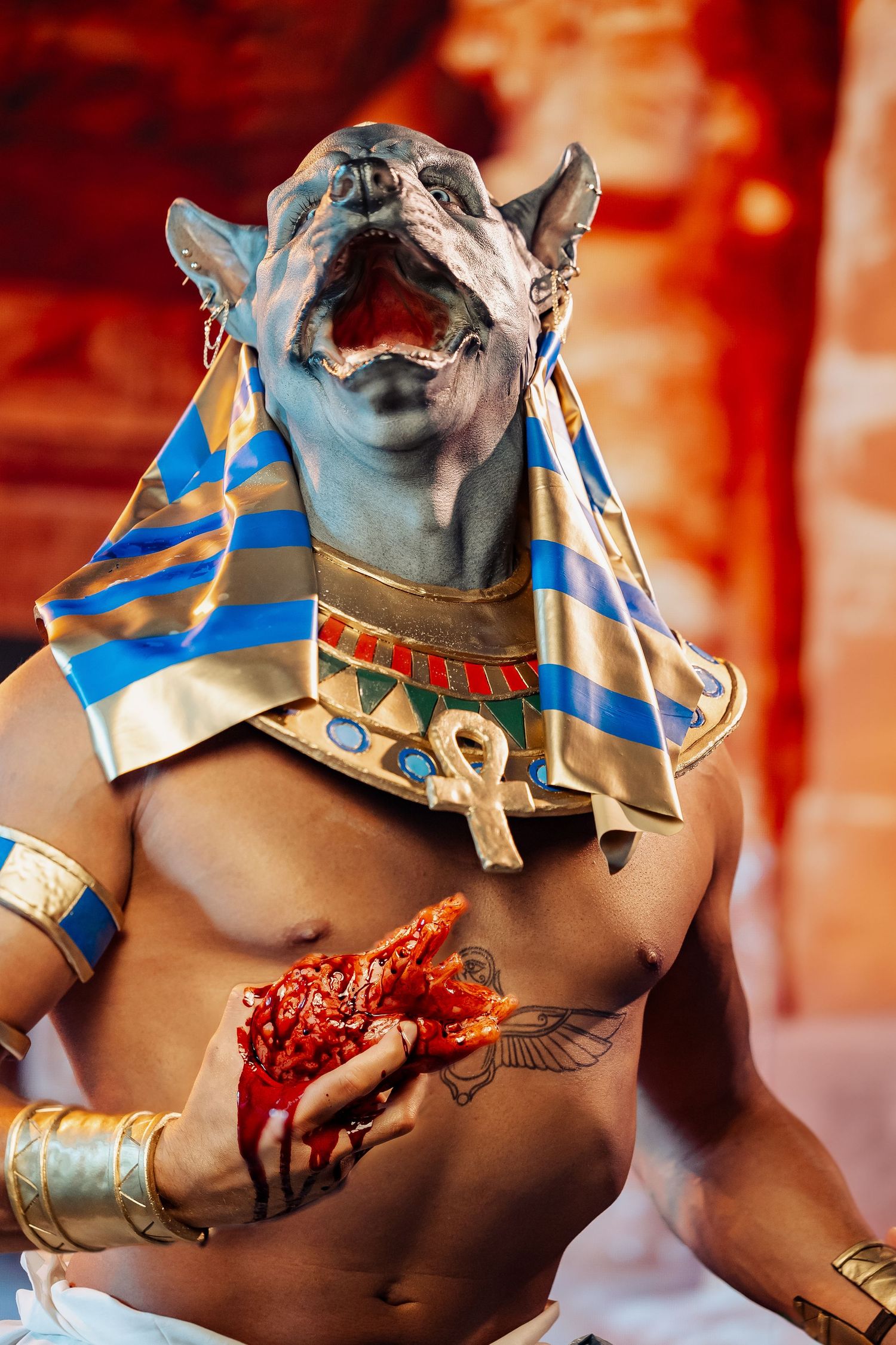 Egyptian-themed Anubis cosplay with blue and gold headdress and ankh necklace holding red crystals.