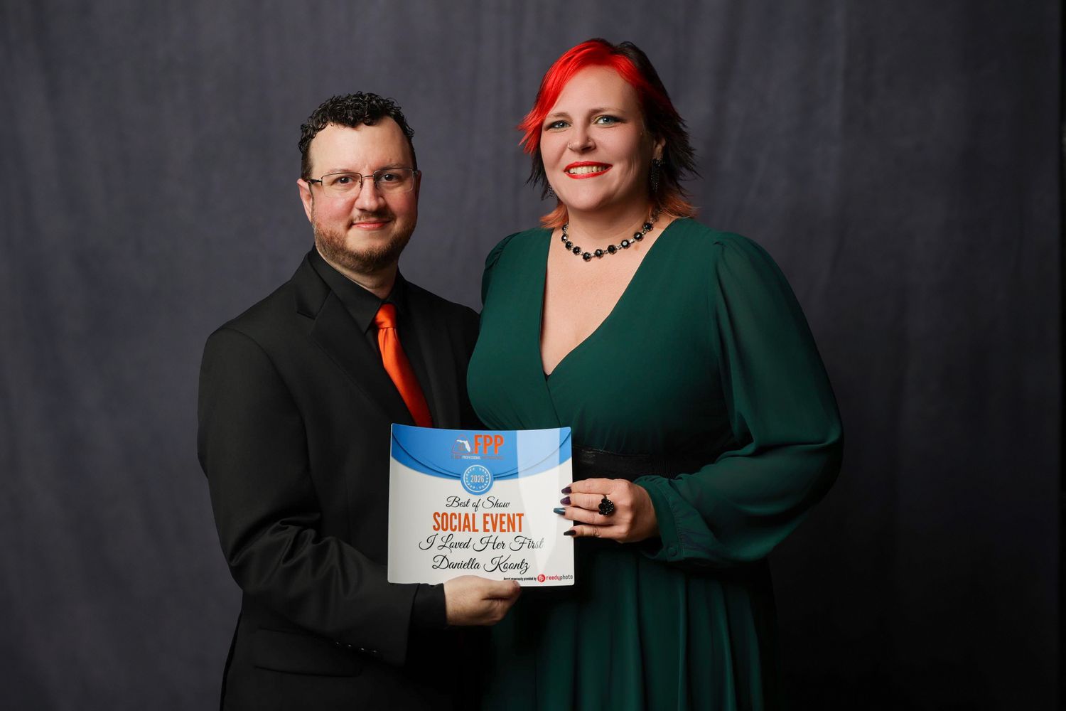 Man and woman in formal attire holding a Social Event award certificate, posing together for a professional photo.