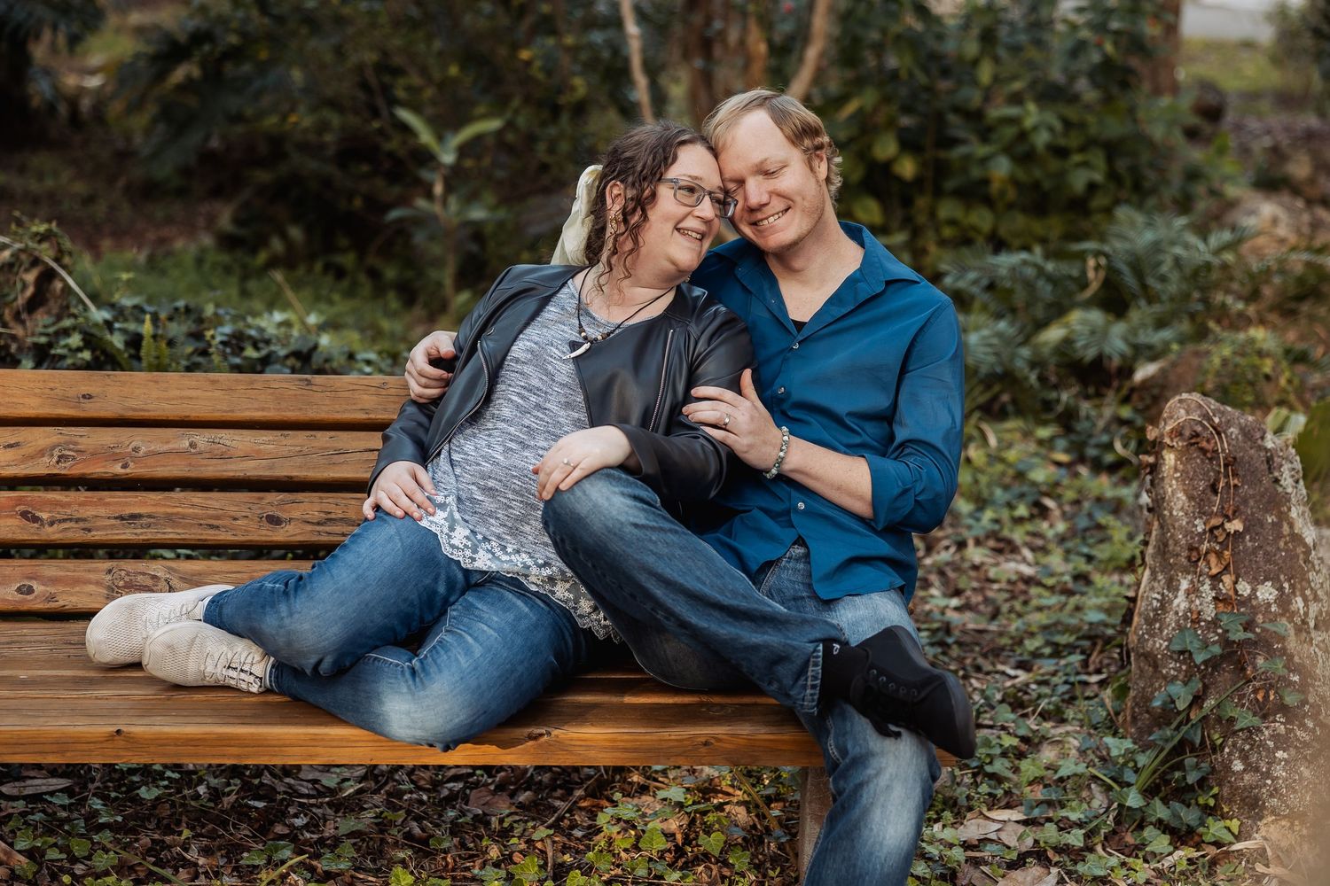 Smiling couple sitting closely together on a wooden bench in a lush garden.