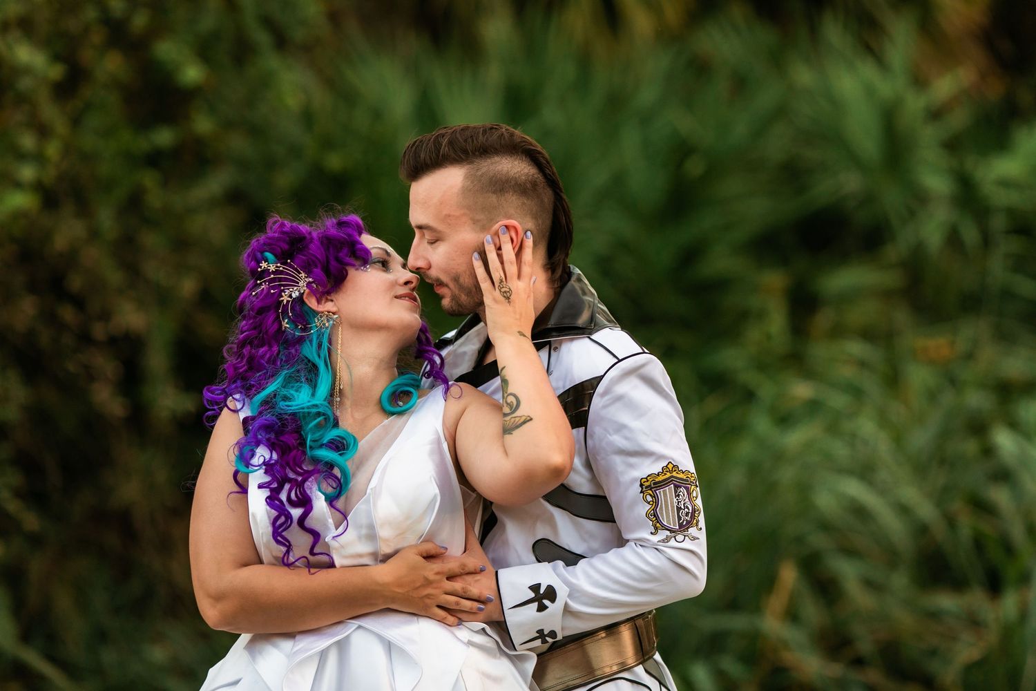 Bride with purple and teal hair kisses groom with mohawk in white vest outdoors.