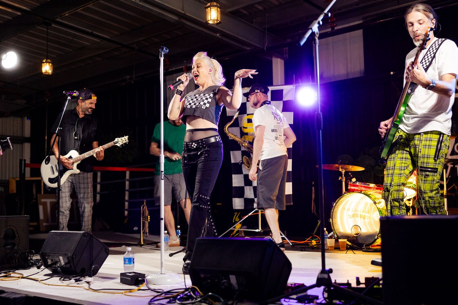 Punk rock band performing on stage with female vocalist and multiple guitarists at outdoor venue.