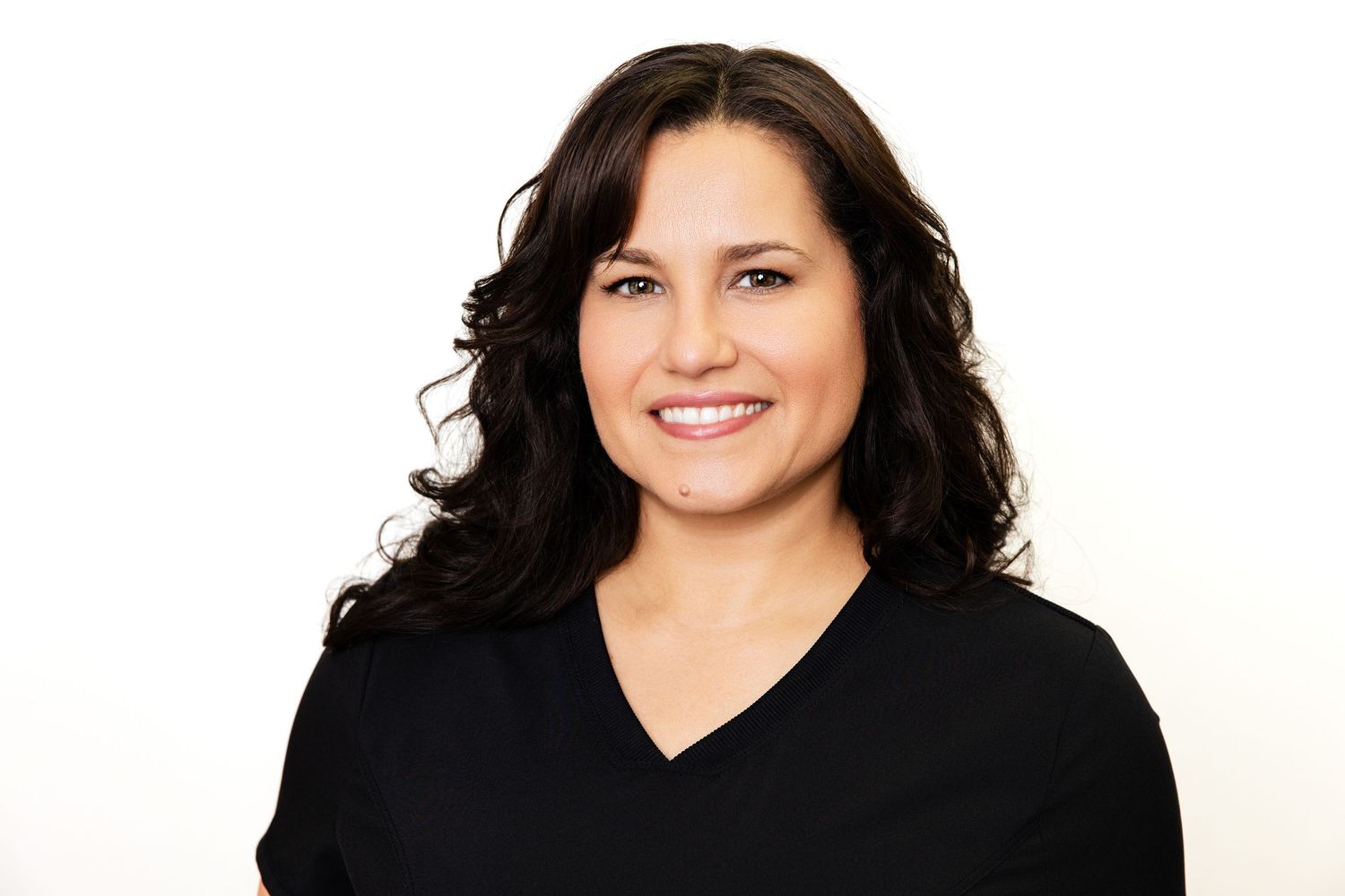 Smiling woman with dark wavy hair wearing black V-neck top against clean white background.