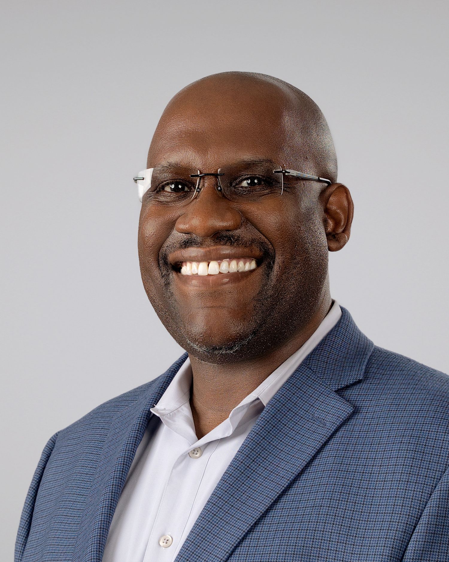 Professional headshot of a smiling bald Black man wearing glasses and a blue blazer.