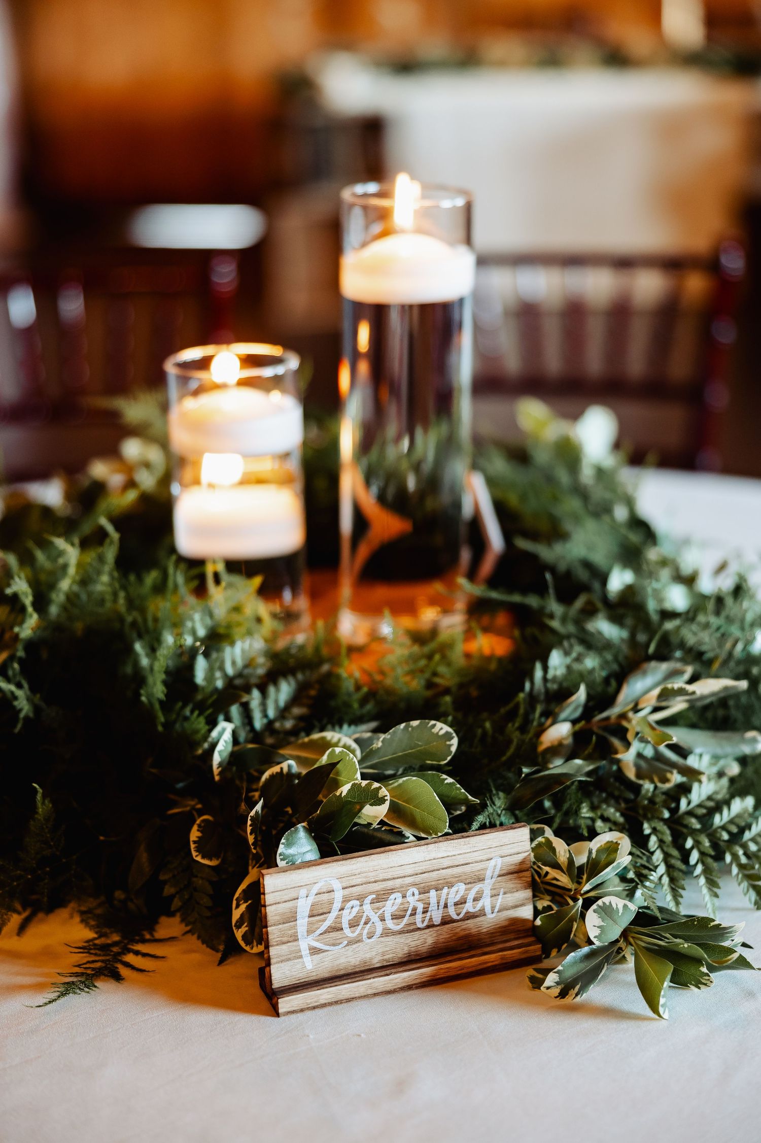 Elegant wedding table centerpiece with floating candles, greenery and a wooden reserved sign.