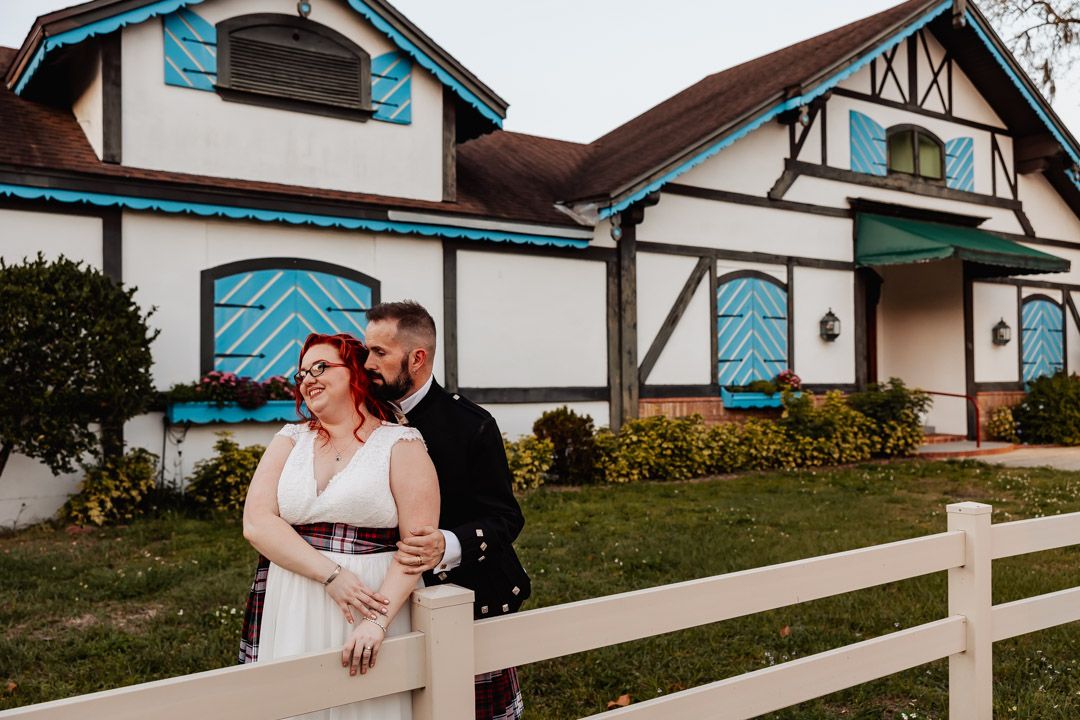 A couple enjoying a quiet moment along a white fence outside their wedding venue.