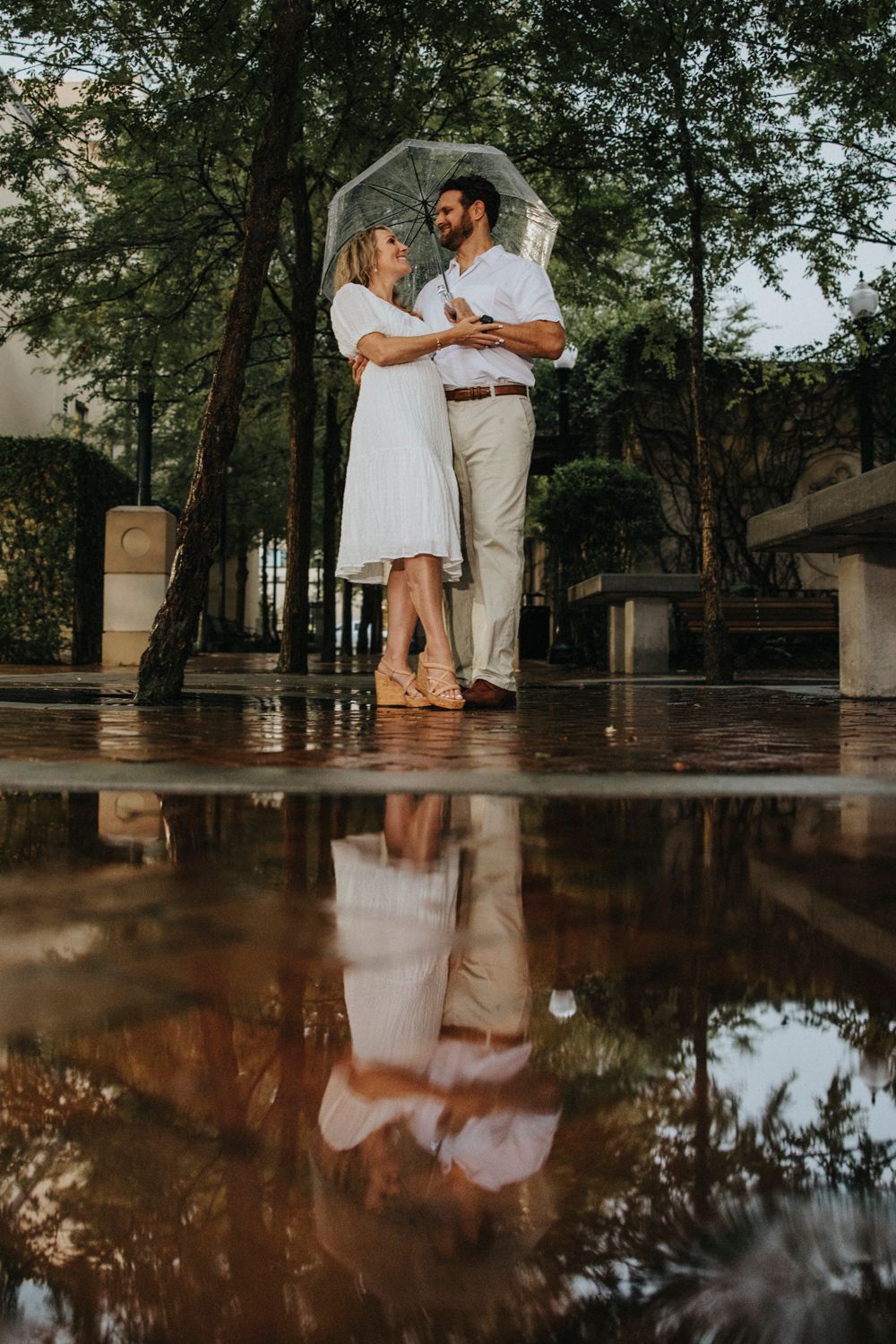 Couple with umbrella dancing in rain with beautiful reflection in puddle.