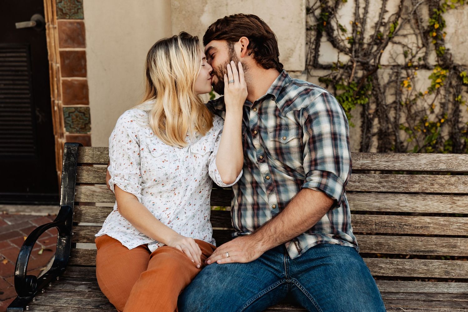 Couple sharing a sweet kiss on an outdoor bench surrounded by vintage architecture.