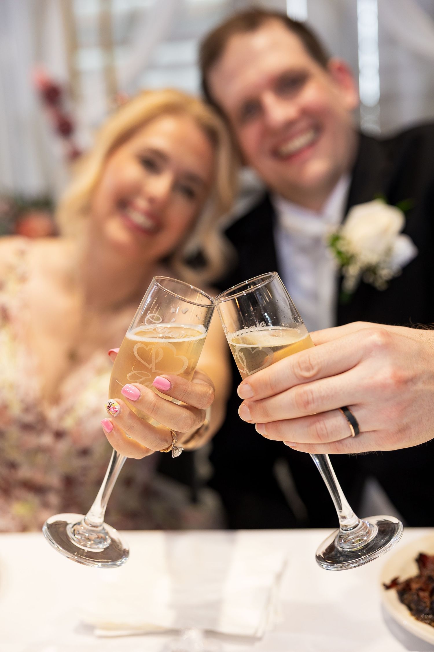 Happy newlyweds toasting with champagne glasses, bride wearing pink nail polish and wedding ring.