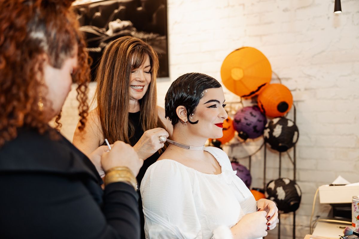 Halloween makeup artist applying face paint to a woman with orange and purple balloons in the background.