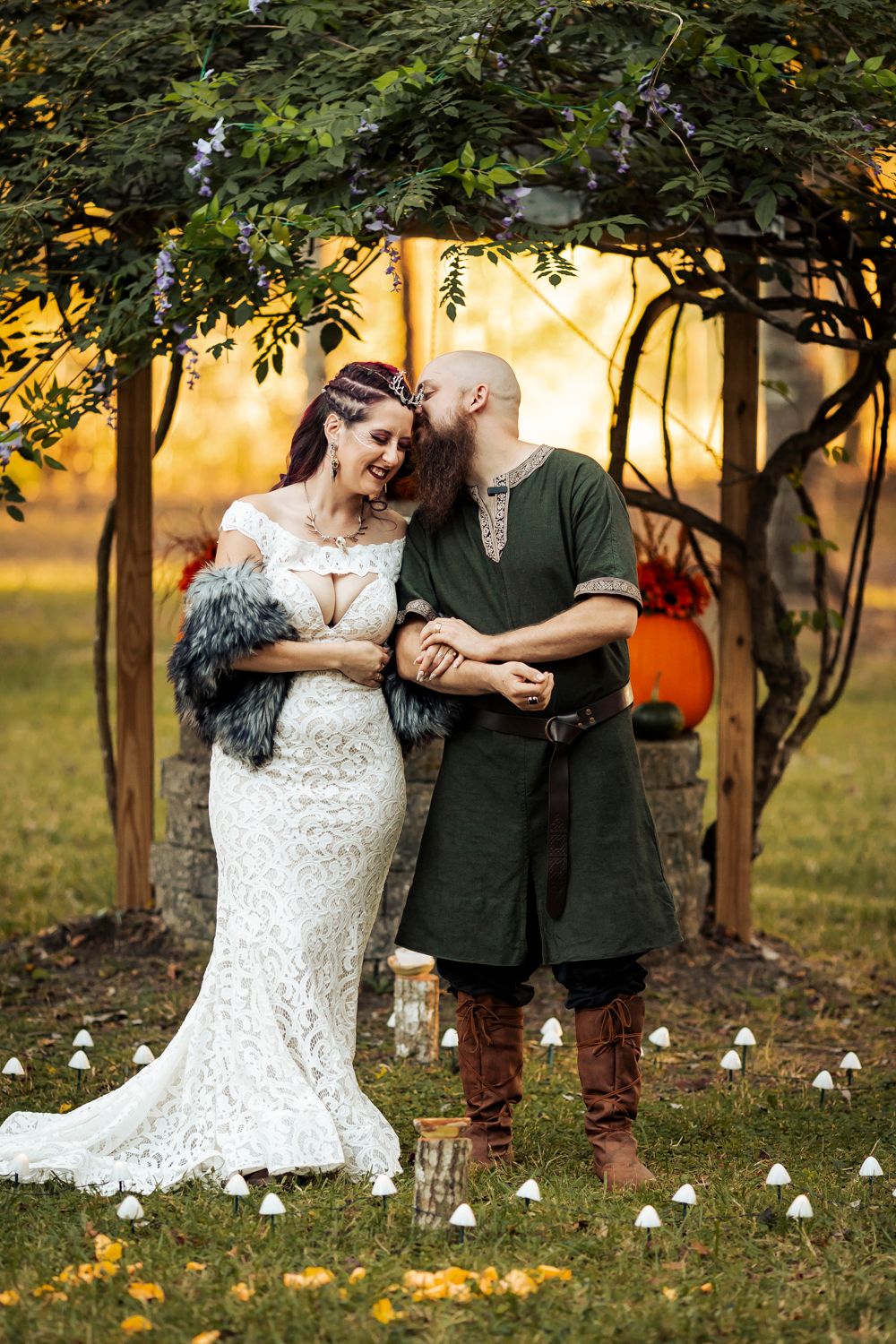 Intimate moment between newlyweds in medieval attire under garden archway with pumpkin decorations.