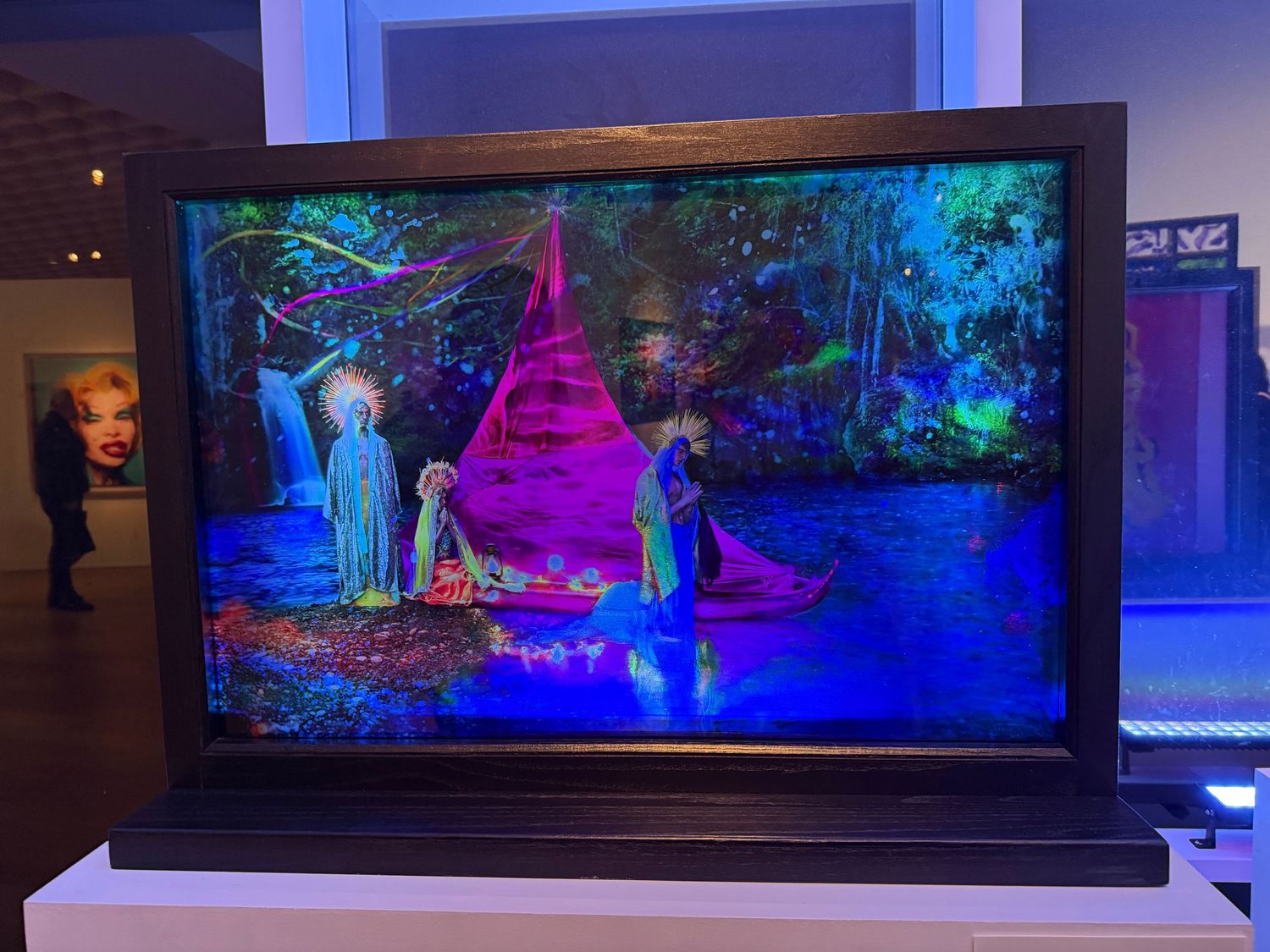 Colorful neon-lit blacklight art installations featuring glowing mushrooms and fantasy landscapes in a gallery setting.